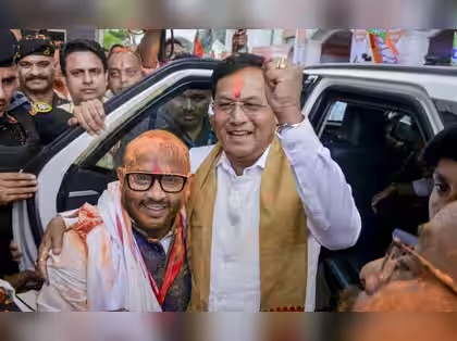 Sarbananda Sonowal, with coloured powder on his forehead, raises a fist beside a smiling supporter
