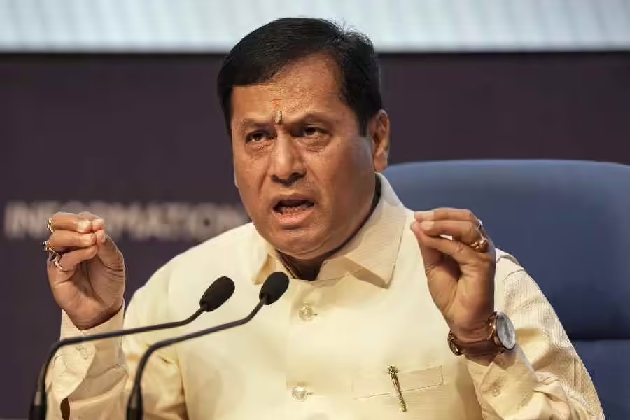 Sarbananda Sonowal gestures with both hands while speaking into microphones at a press briefing